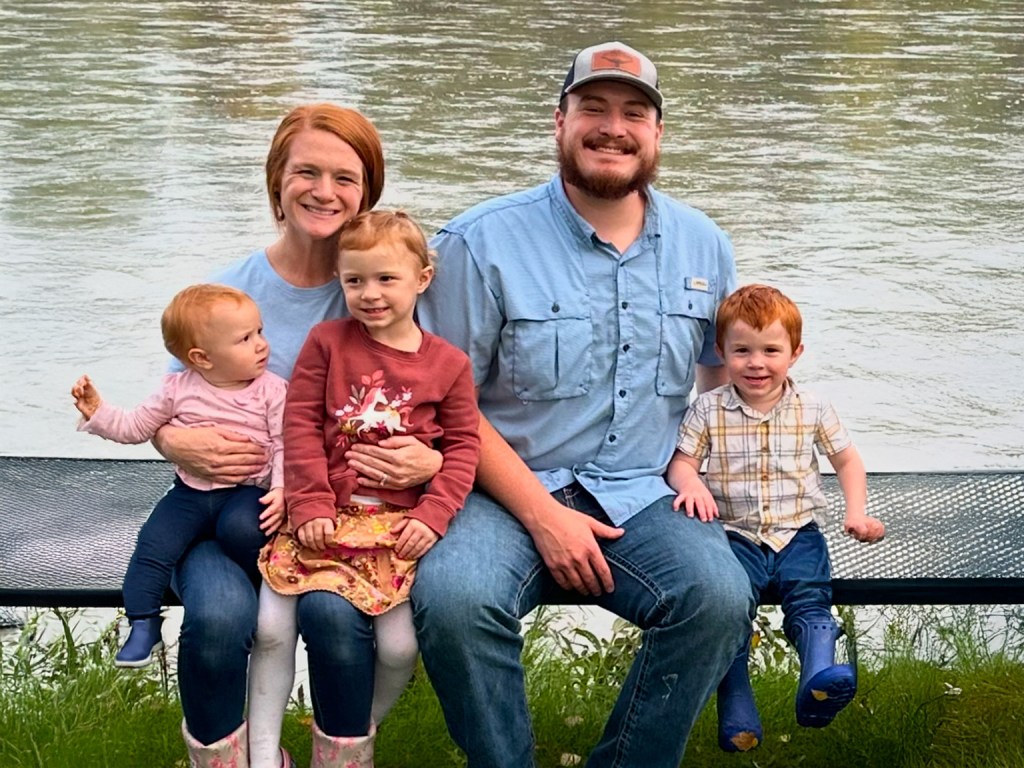 A smiling family sitting on a bench by the Kenai River in Cooper Landing, Alaska, enjoying a scenic outdoor setting.